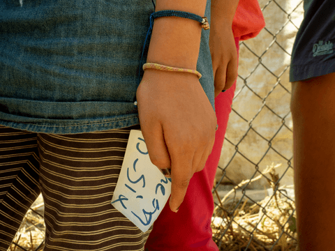 Atena holds a piece of paper indicating the number of empty bottles she returned, commensurate to the number she will receive in return.