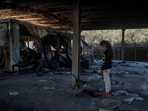 Manija is greeted by a cat while walking through the burnt-out site of Moria Reception and Identification Centre.