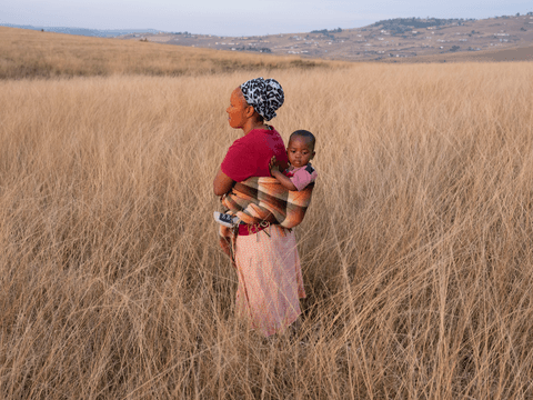 Thandeka and her son, Indamkele, stand in the field outside their home.