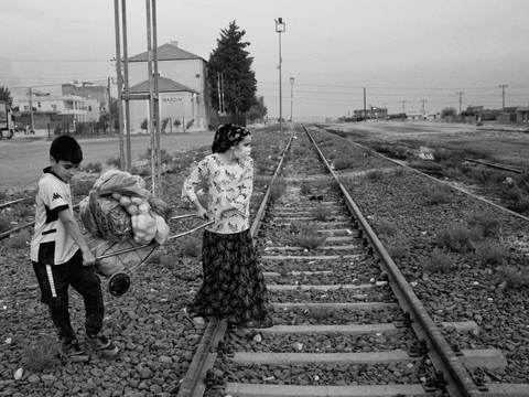 Asaf (left), 12, helps his mother cross train tracks as they return home with food.